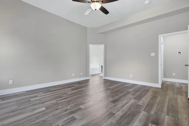 an empty room with wooden floor ceiling fan and window