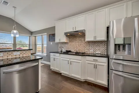 a kitchen with granite countertop a refrigerator a sink and white cabinets