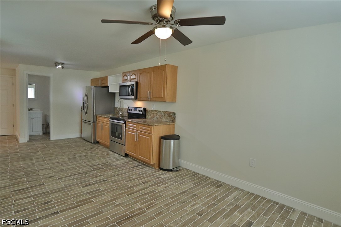11 California Road Lehigh Acres, FL 33936 - Photo 9 of 19 an empty room with wooden floor a ceiling fan a kitchen view and a refrigerator