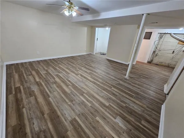 a view of an empty room with wooden floor and a ceiling fan