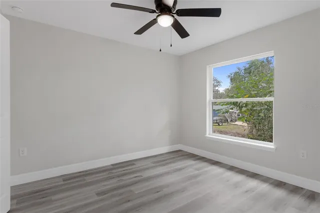 an empty room with wooden floor windows and ceiling fan