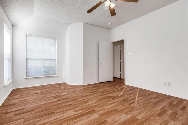an empty room with wooden floor chandelier fan and windows