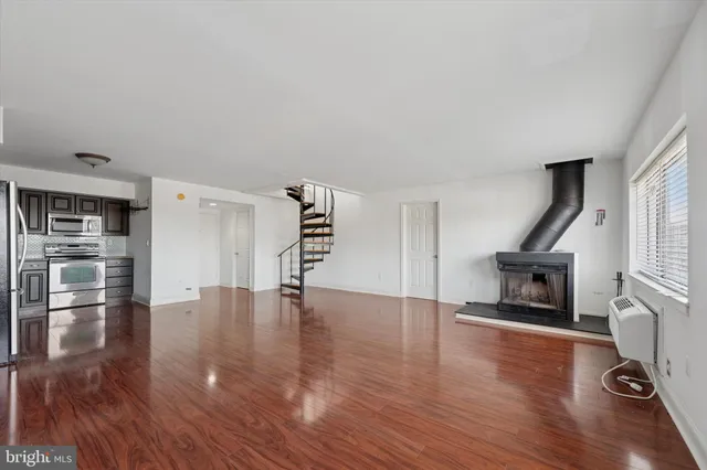 a view of an empty room with wooden floor fire place and windows