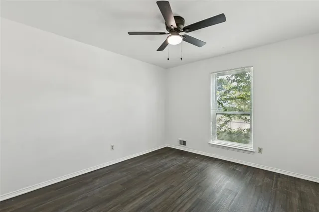 an empty room with wooden floor ceiling fan and windows