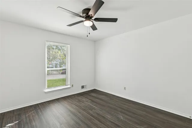 an empty room with wooden floor fan and windows