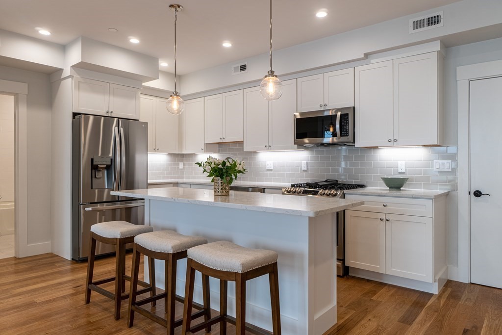 a kitchen with stainless steel appliances a stove a sink a microwave a refrigerator and white cabinets