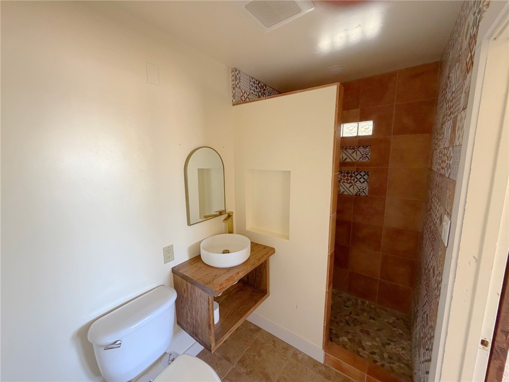 15691 Apache Loop Ehrenberg, AZ 85334 - Photo 11 of 24 Bathroom featuring a walk-in shower with mosaic tile accents, a stone pebble shower floor, and a white round vessel sink with a gold-tone faucet
