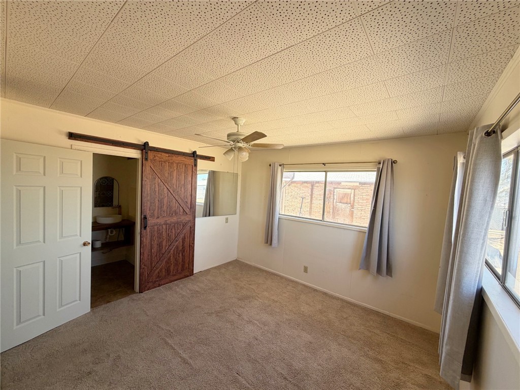 15691 Apache Loop Ehrenberg, AZ 85334 - Photo 12 of 24 Carpeted room featuring a wood barn door, paneled ceiling, ceiling fan, and multiple windows
