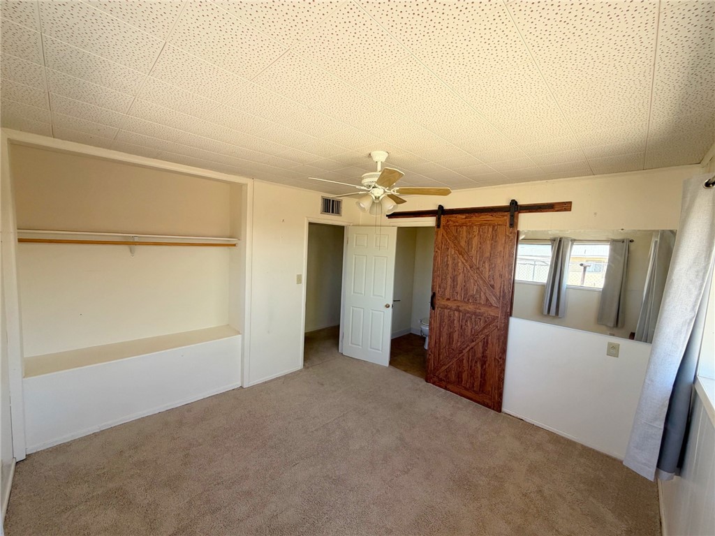 15691 Apache Loop Ehrenberg, AZ 85334 - Photo 14 of 24 Bedroom featuring a sliding barn door, ceiling fan, carpeting, built-in open closet with shelving, and windows with curtain rods