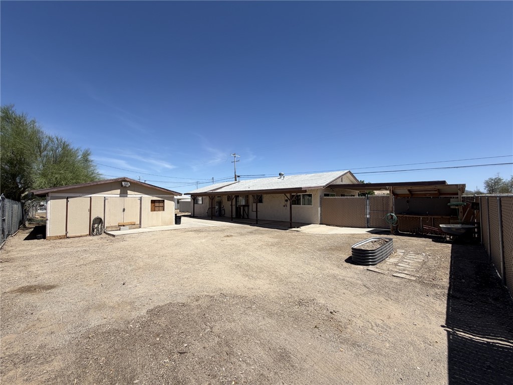 15691 Apache Loop Ehrenberg, AZ 85334 - Photo 23 of 24 Expansive rear yard featuring an accessory building with multiple doors, a covered patio area, and a metal raised garden bed
