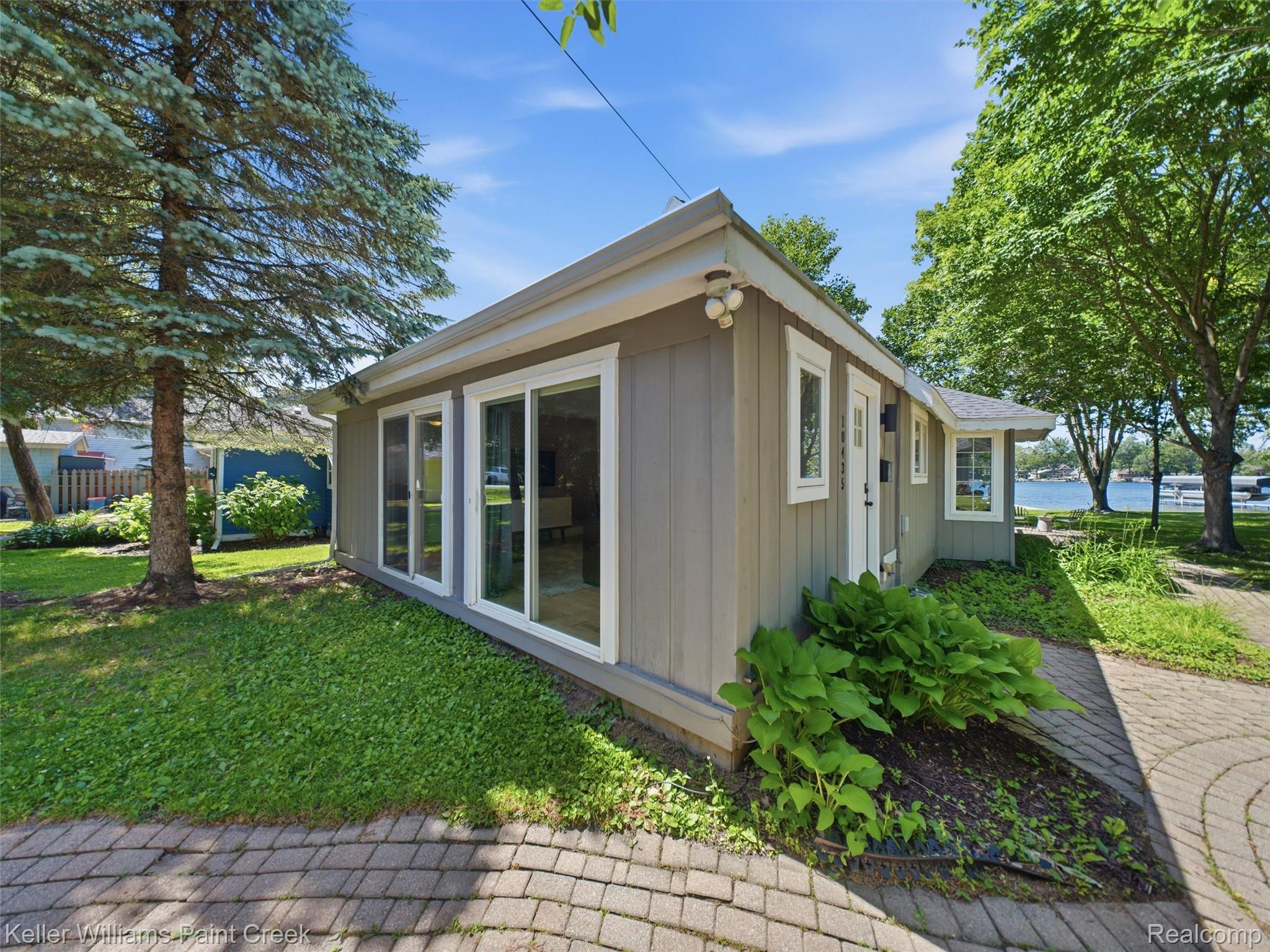 10435 Spring Street Fenton, MI 48430 - Photo 38 of 40 Gray-sided single-story residence featuring multiple white-framed sliding glass doors and an adjacent paver pathway