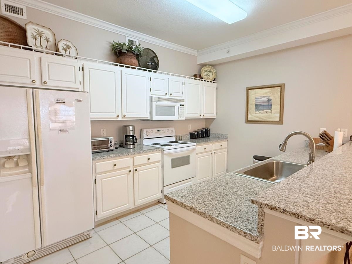 27284 Gulf Road, Unit 212 Orange Beach, AL 36561 - Photo 8 of 35 Kitchen featuring white appliances, ornamental molding, white cabinetry, light tile patterned flooring, and light stone countertops