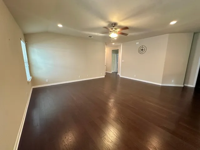 an empty room with wooden floor fan and windows