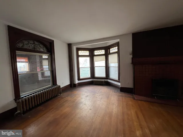 a view of an empty room with wooden floor fireplace and a window