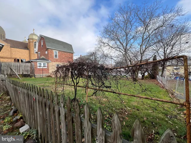 a view of a white house with a small yard and wooden fence