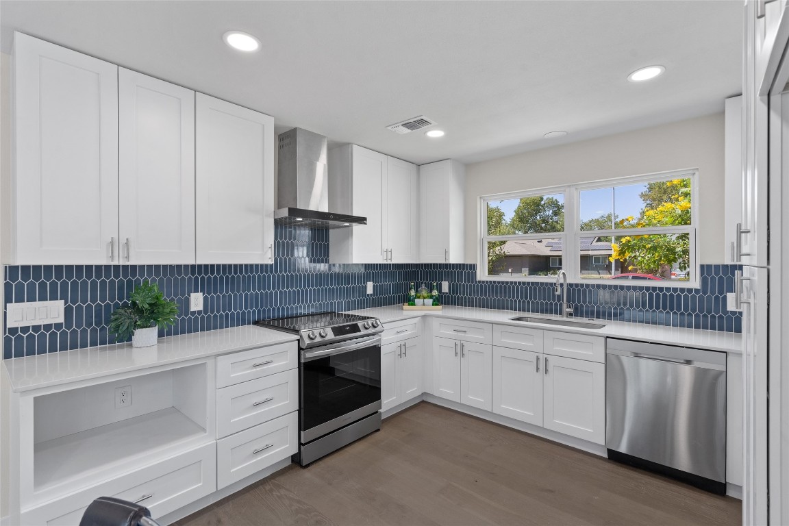 6901 Windrift Way Austin, TX 78745 - Photo 23 of 30 Kitchen with appliances with stainless steel finishes, wall chimney exhaust hood, white cabinets, light stone counters, and dark wood-style flooring