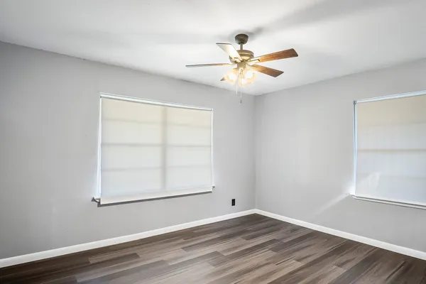 an empty room with wooden floor fan and windows