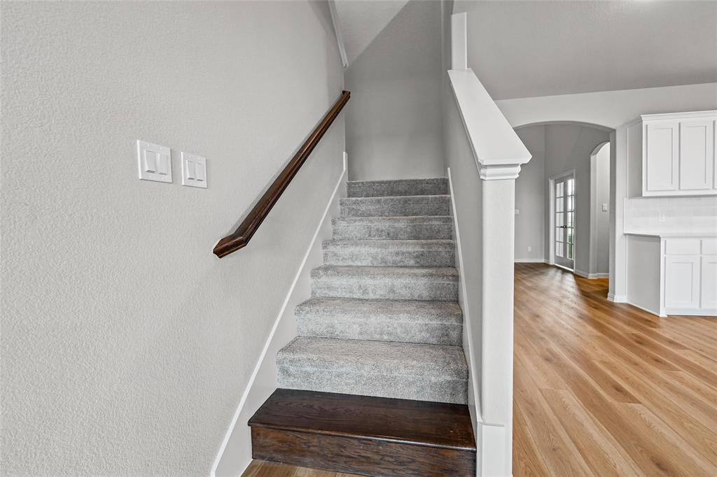 1205 Colca Drive Springtown, TX 76082 - Photo 25 of 37 Carpeted staircase with a wood-finish handrail, wood-finish flooring, and white cabinetry