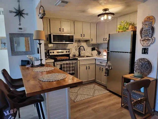 a kitchen with stainless steel appliances granite countertop a refrigerator a stove top oven a sink dishwasher and white cabinets with wooden floor