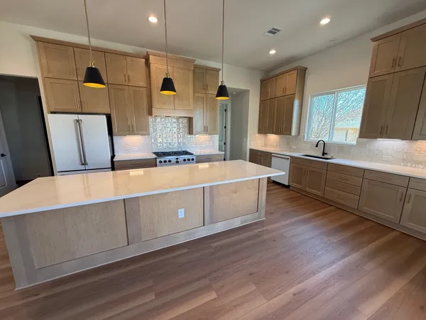 a large kitchen with stainless steel appliances a large counter top a sink a refrigerator and window