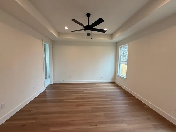 an empty room with wooden floor a ceiling fan and windows