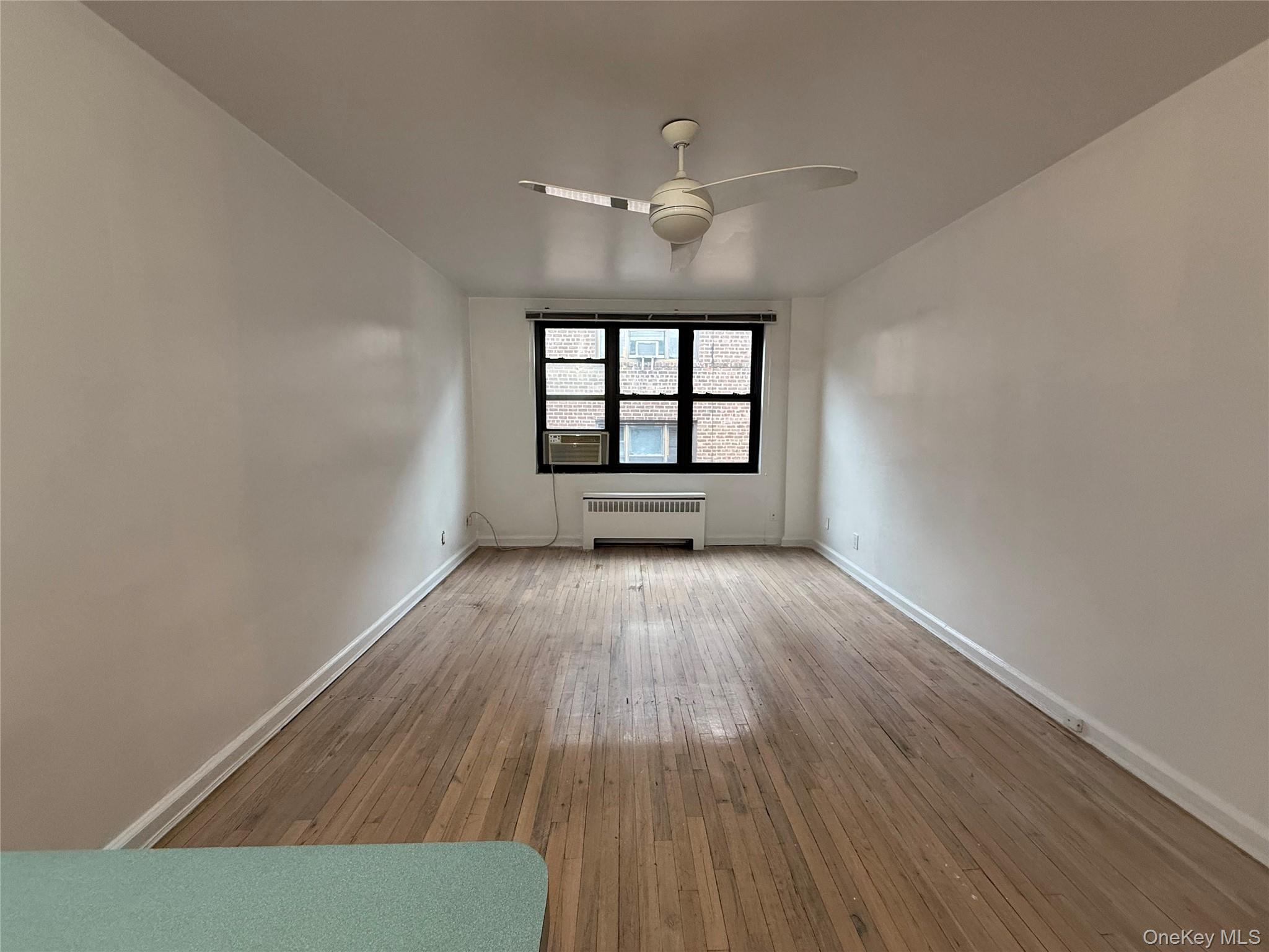 15 Canterbury Road, Unit D13 Great Neck, NY 11021 - Photo 4 of 10 Empty room with light wood-style flooring, radiator heating unit, and ceiling fan