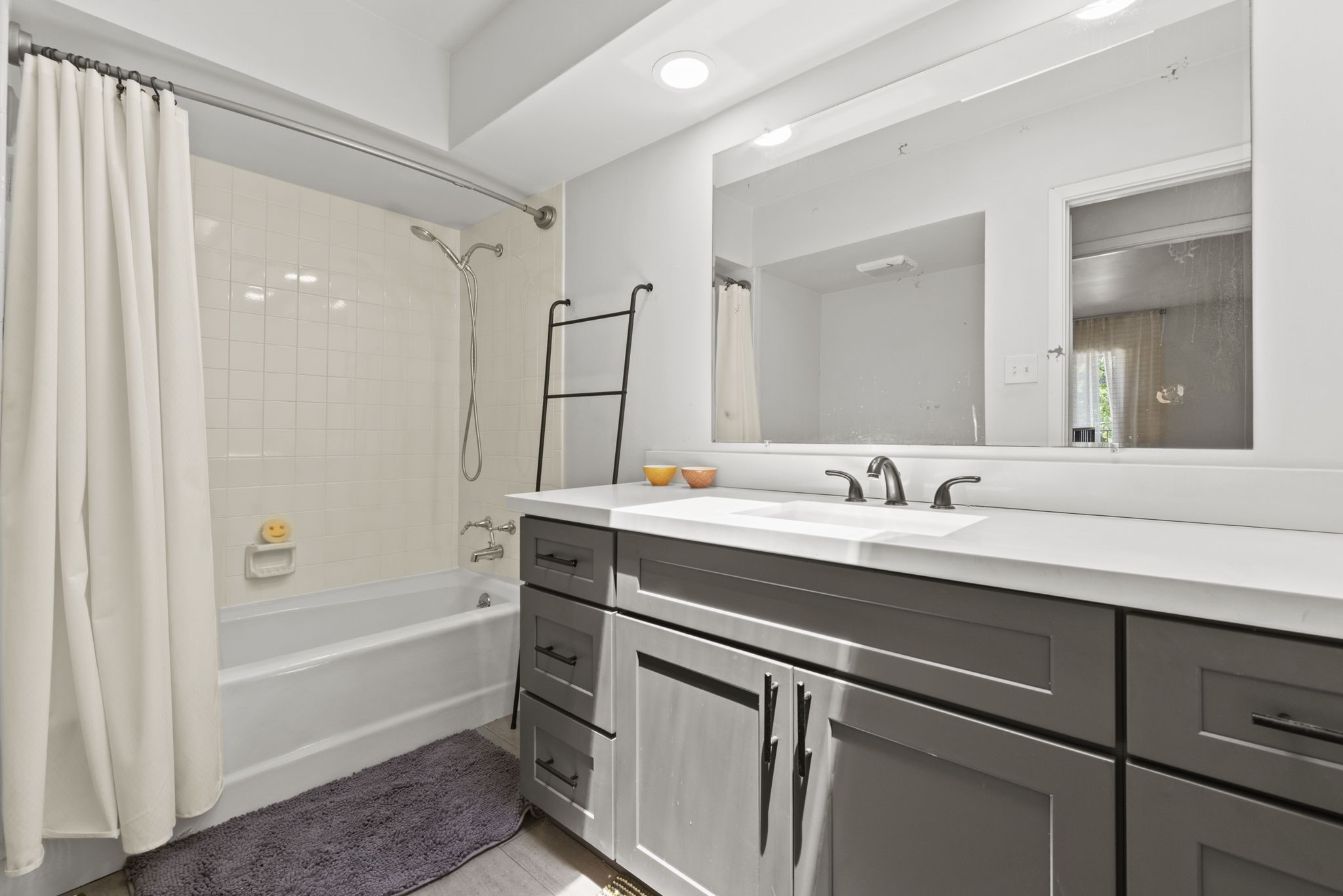 1115 Augusta Drive, Unit 26 Houston, TX 77057 - Photo 13 of 23 Modern full bath featuring dual sinks, dark gray cabinetry, and a tile-surround tub — complete with recessed lighting and a ladder-style towel rack for added style.