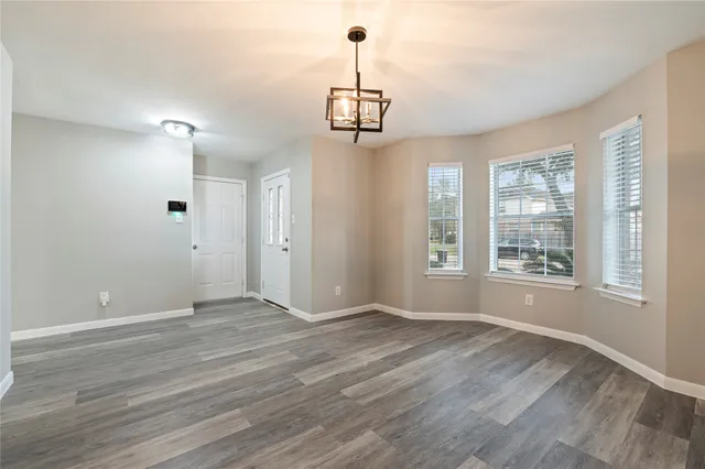 a view of an empty room with wooden floor and a kitchen