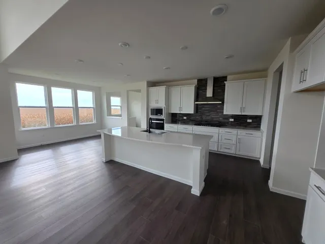 a large open kitchen with stainless steel appliances granite countertop a stove a sink a refrigerator white cabinets and wooden floor