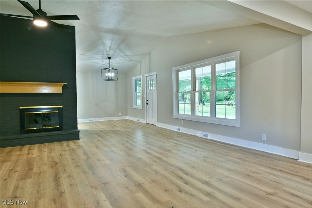 7655 Connelly Road Masury, OH 44438 - Photo 16 of 46 Unfurnished living room with lofted ceiling, wood finished floors, a fireplace, a chandelier, and a ceiling fan