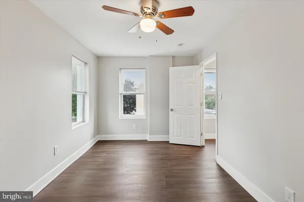 an empty room with wooden floor chandelier fan and windows