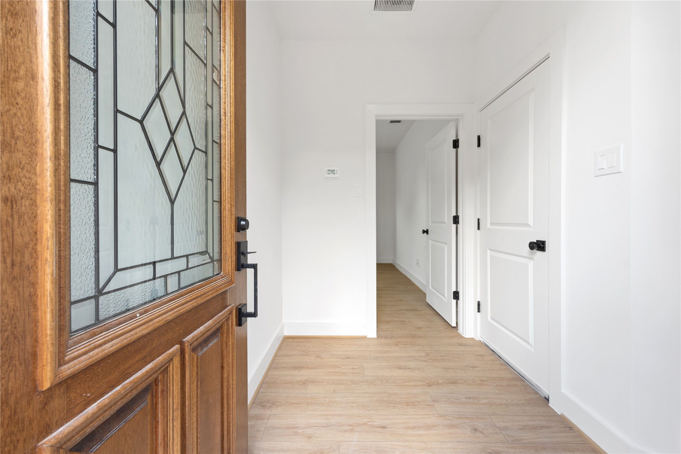 2121 Hoskins Drive, Unit C Houston, TX 77080 - Photo 6 of 34 A welcoming entry sets the tone with a warm wood front door featuring decorative glass, crisp white walls, black hardware, and light wood-look flooring. The bright foyer offers a clean modern first impression, with nearby storage and easy access into the home’s flexible first-floor layout.