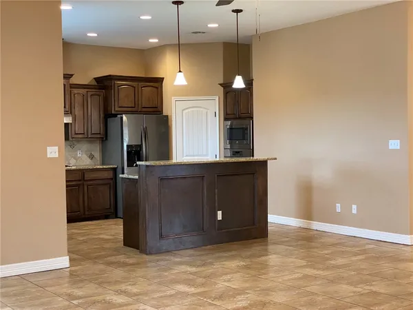 a kitchen with stainless steel appliances kitchen island granite countertop a refrigerator and a wooden floor