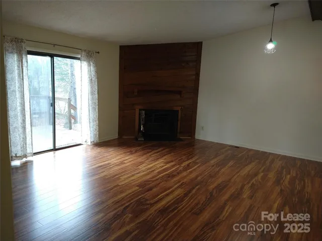 an empty room with wooden floor fireplace and windows