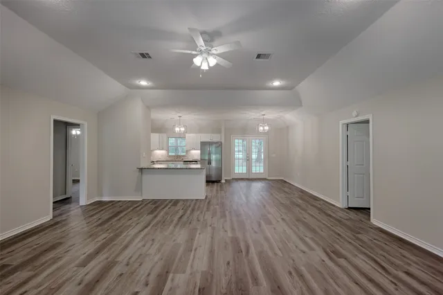 a view of an empty room and kitchen with wooden floor
