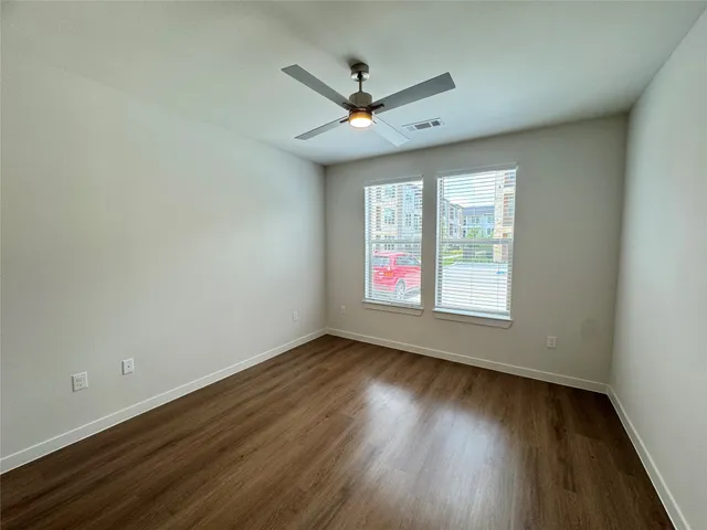 an empty room with wooden floor fan and windows
