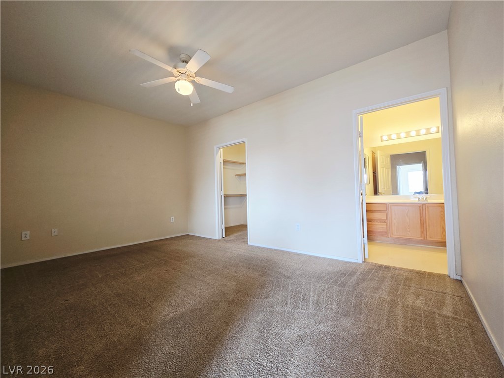 9580 West Reno Avenue, Unit 283 Las Vegas, NV 89148 - Photo 7 of 19 Unfurnished bedroom with dark carpet, a walk in closet, a ceiling fan, and ensuite bath