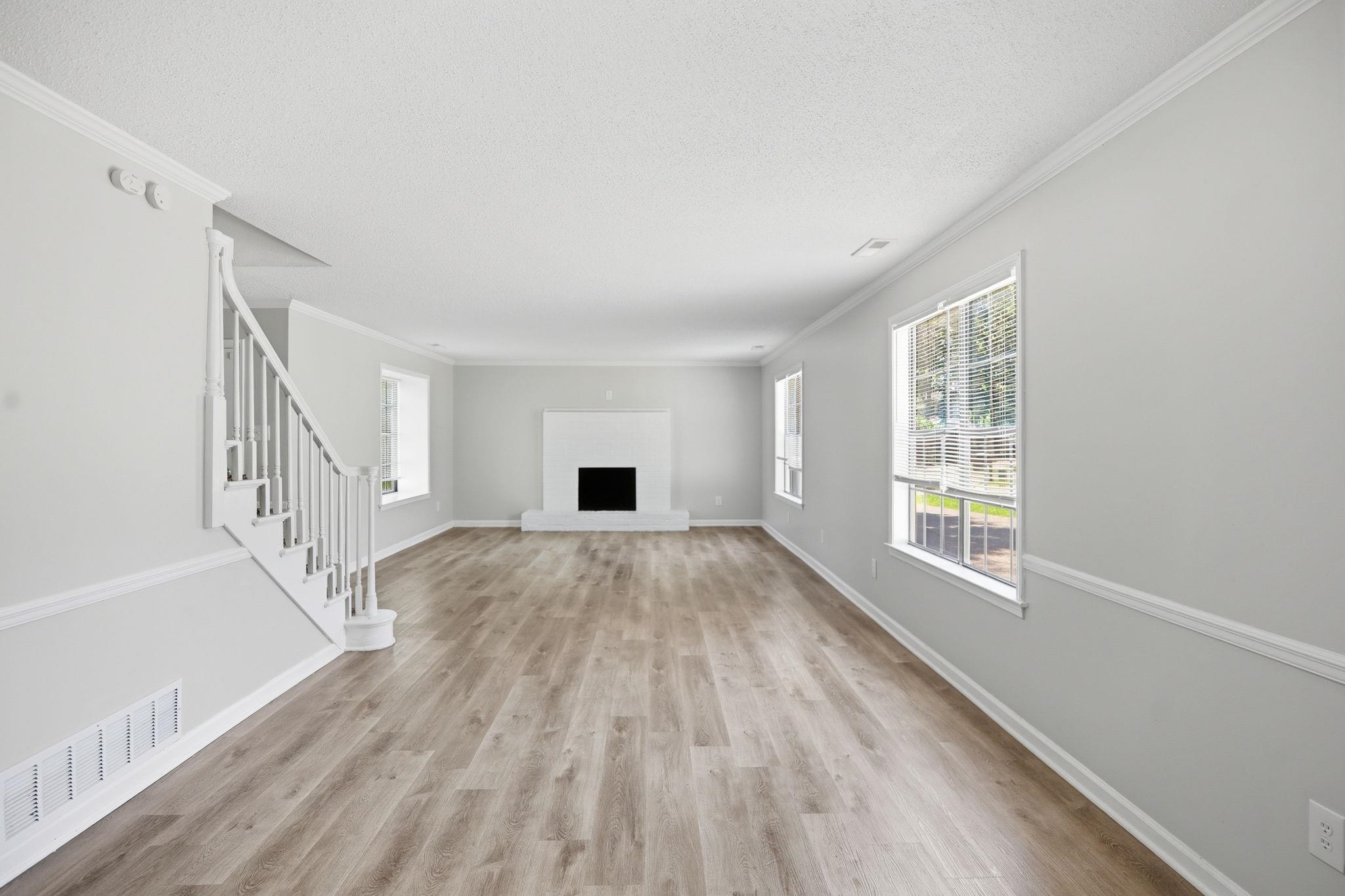 3113 Raleigh Ridge Cove Memphis, TN 38128 - Photo 3 of 38 Bright living area featuring wood-finish flooring, a white mantel fireplace, multiple large windows, a white staircase with balusters, and elegant crown molding throughout