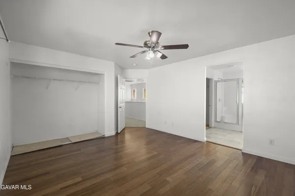 an empty room with wooden floor ceiling fan and windows