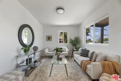 a living room with furniture a mirror potted plant and a large window