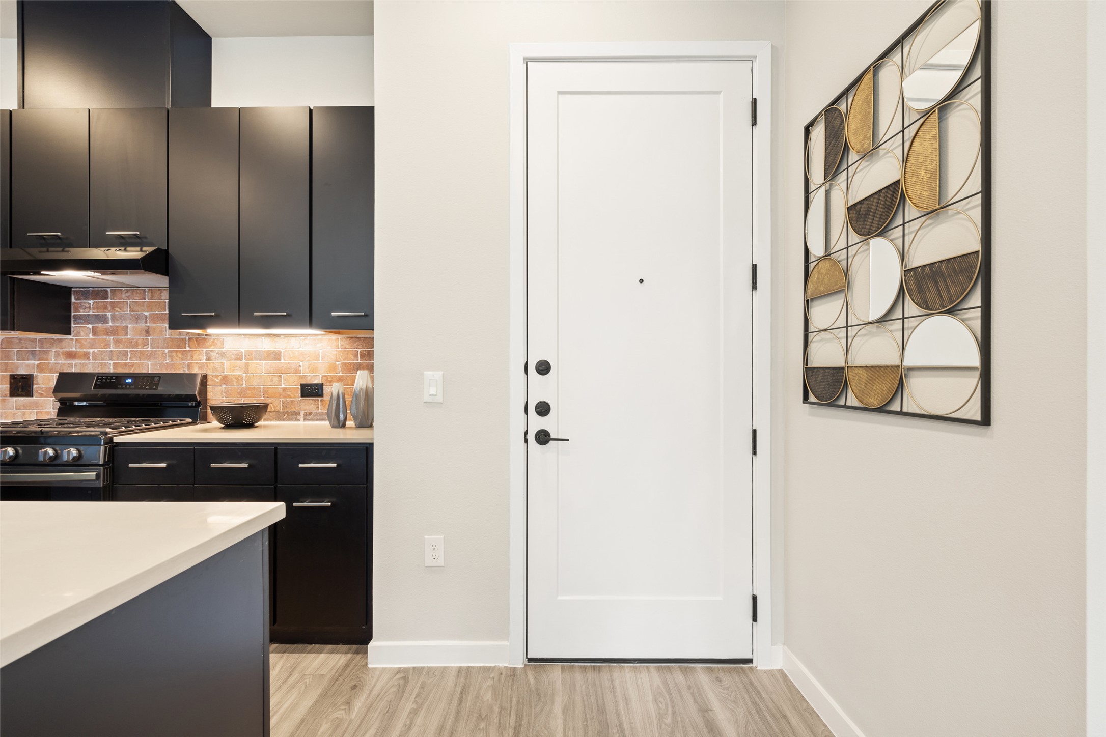 4510 Terry-O Lane, Unit 341 Austin, TX 78745 - Photo 4 of 40 Kitchen with dark cabinetry, light countertops, and a brick-style backsplash, featuring a range with an overhead exhaust fan