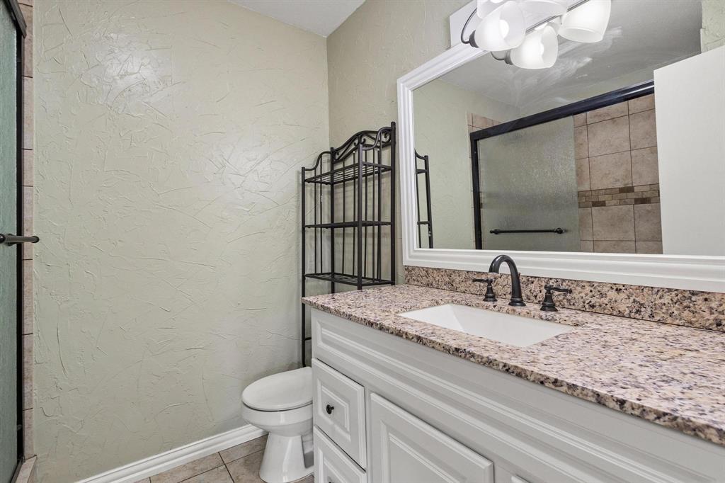 1223 Yowell Road Whitesboro, TX 76273 - Photo 17 of 30 a bathroom with a granite countertop toilet sink and mirror
