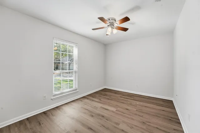 an empty room with wooden floor chandelier fan and windows