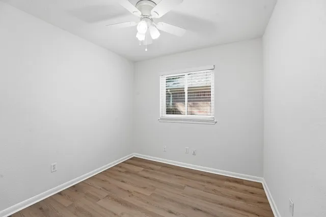 an empty room with wooden floor chandelier fan and window