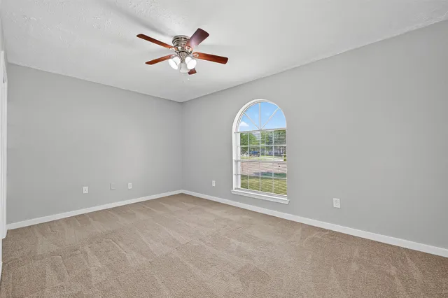 an empty room with ceiling fan and windows