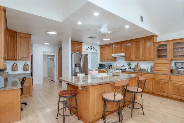 a kitchen with stainless steel appliances granite countertop a stove top oven a sink a refrigerator and white cabinets with wooden floor