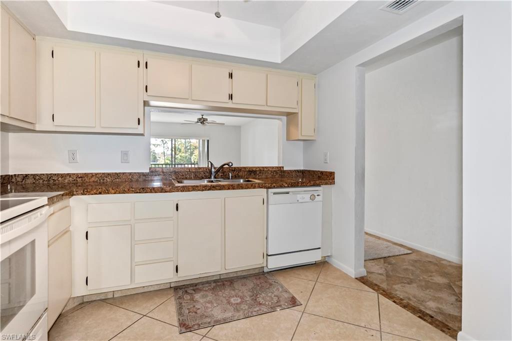 1733 Courtyard Way, Unit 204 Naples, FL 34112 - Photo 5 of 15 Kitchen featuring white appliances, cream cabinetry, a ceiling fan, a tray ceiling, and light tile patterned flooring