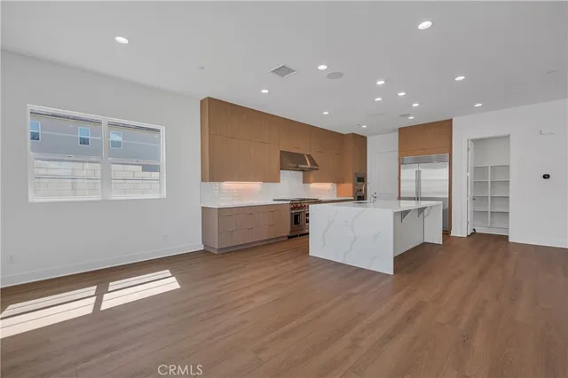 a large white kitchen with kitchen island a sink dishwasher a refrigerator and white cabinets with wooden floor