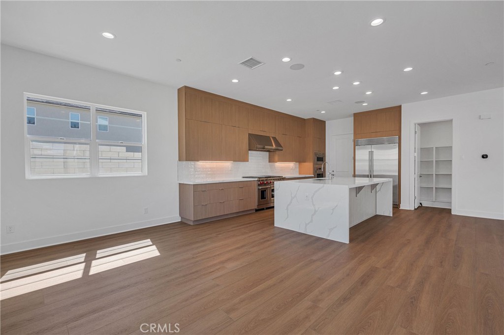 27510 Elderberry Drive Valencia, CA 91381 - Photo 18 of 60 a large white kitchen with kitchen island a sink dishwasher a refrigerator and white cabinets with wooden floor