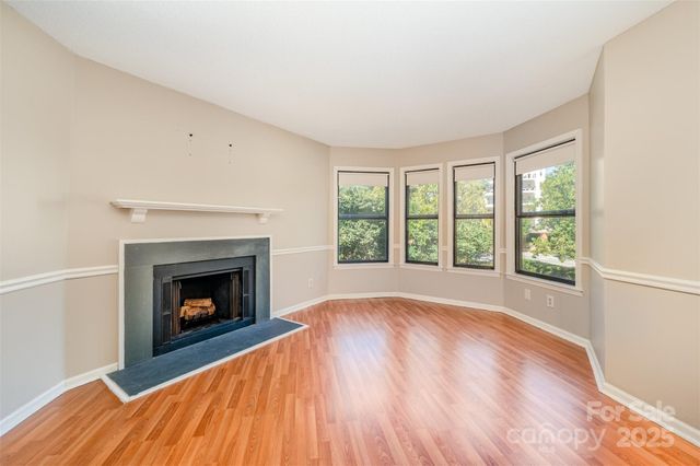 a view of an empty room with wooden floor fireplace and a window